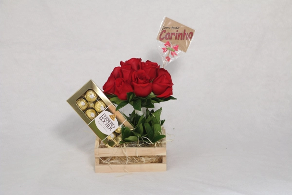 Arreglo de regalo con rosas rojas, bombones y una tarjeta que dice “Com todo carinho”.